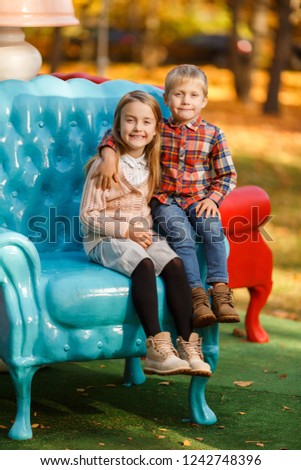 Picture of girl and boy sitting on blue armchair in autumn park