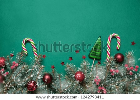 Christmas composition of tree branches, candy cane and red glass balls on green background with copy space. Top view. Holiday card.