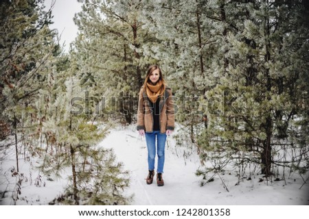 Outdoor close up portrait of young beautiful happy smiling girl wearing scarf and gloves in forest. Model posing in a snowy park. Winter holidays concept. Frost winter walks season.
