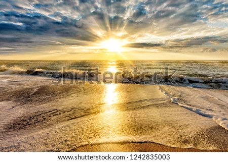 scenic sunset over stormy sea beach with setting sun rays coming through dramatic clouds on orange blue sky reflecting on water panoramic aerial nature dusk atmosphere evening landscape background