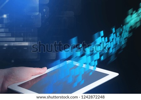 Hand of man holding tablet computer over dark blue background with double exposure of blue flow of data and business infographics. Toned image