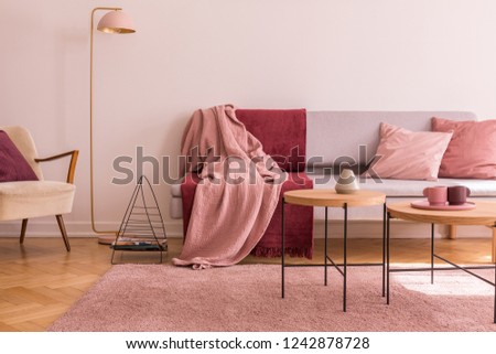 Wooden table on pink carpet in front of grey settee in living room interior with lamp. Real photo