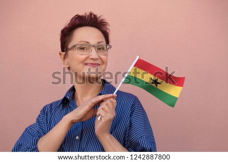 Ghana flag. Woman holding Ghana flag. Nice portrait of happy middle aged lady 40 50 years old with a national flag over pink wall background on the street outdoors.