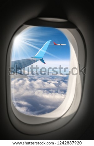 Two commercial airplanes (aircraft wing and plane) photographed through the porthole window, while flying above the clouds.