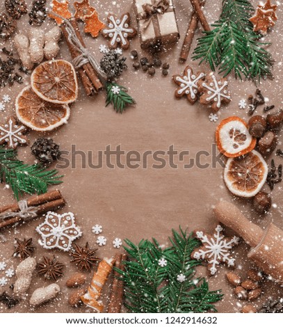 Frame with fir branches, Gingerbread cookies and Christmas decorations on dark brown paper background. Top view.