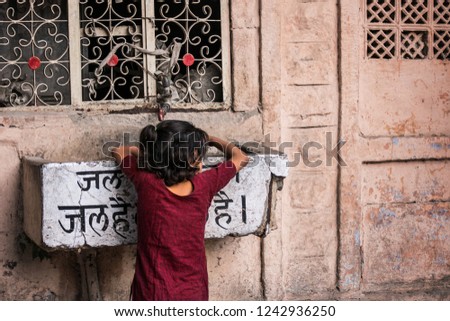 Young Indian girl taking water on the street. Translation of hindi writing: "Water is life".