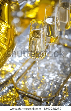 Close up of shiny glasses of champagne over black, white, golden and silver balloons background