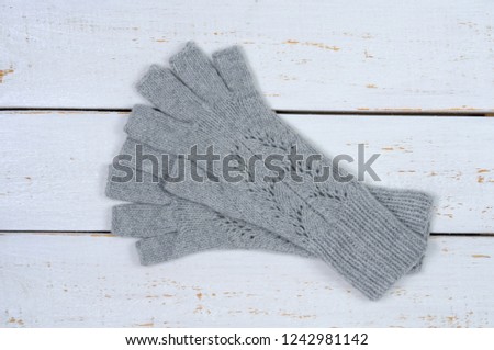 Knitted gray gloves with open fingers on a white wooden background. Handwork. View from above.