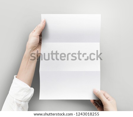 Hand holding empty white blank paper sheet A4 size on grey background.