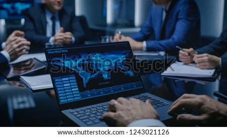 On the Table Laptop Showing World Data Flow: Team of Politicians, Corporate Business Leaders and Lawyers Sitting at the Negotiations Table in the Conference Room, Trying to Come to an Agreement. Royalty-Free Stock Photo #1243021126