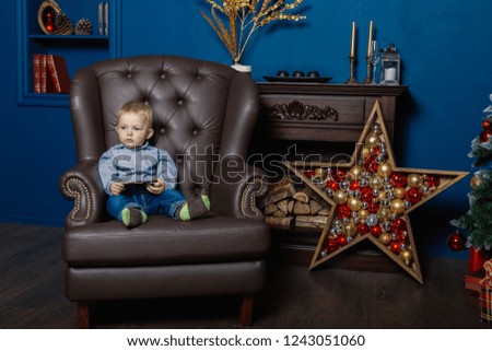 A little boy is sitting in an old leather chair with a phone.