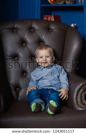 A little boy is sitting in an old leather chair.