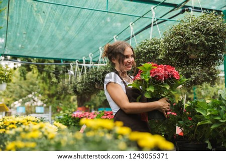 Happy young woman working in a greenhouse, holding a flower pot