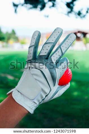 A hand of female golfer with a glove and red ball, close up. Green golf courses on the background.