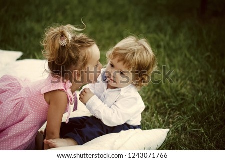 Brother and sister play on summer day outdoor. Girl kiss boy with blond hair on green grass. Family, love, trust concept. Vacation, leisure, lifestyle. Innocence, children, childhood.