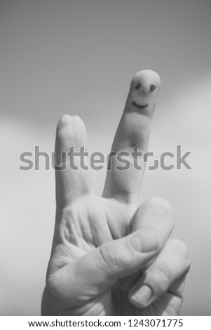 Closeup of one human hand of small kid holding raised palm with painted smile on injured forefinger in piece gesture sunny day outdoor on blue sky with white clouds background, vertical picture