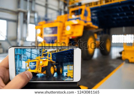 Man makes a picture with his mobile phone. Big mining truck in the production shop of the car factory. 