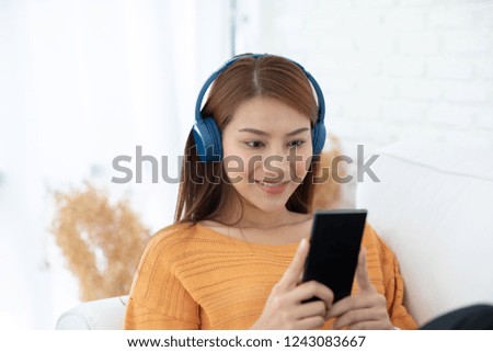 Beautiful Attractive Asian young woman listen music lying on sofa and using smartphone to playing social media in living room feeling so relax and comfortable in holiday,Selective Focus