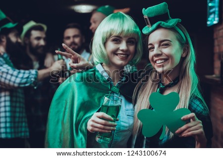 Saint Patrick's Day Party. Friends is Celebrating. Happy People is Drinks a Green Beer. Friends is Men and Women. Girl Holding a Clover and Showing Victory Sign. People in a Green Hats. Pub Interior.