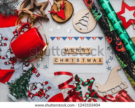 Christmas card. Colorful Christmas decorations and toys, warm socks with Santa Claus, red mug and ribbon on a white, wooden surface. Merry Christmas. Top view, close-up, flat lay