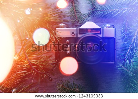Top View of Vintage Camera Between Christmas decorations, Christmas tree, warm and cold toning, lights, garlands, bokeh on Wooden Texture