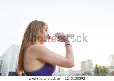 Sports girl in the tops drinking water from the bottle on the street after doing sports. Sports concept. Water and fitness. Copyspace