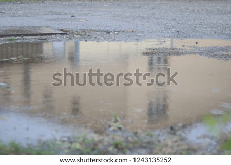 Puddle on the ground close up with house reflection in it. Wet soil in a field. 