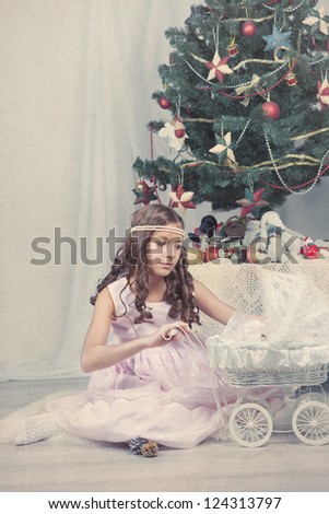 Nice girl plays with doll around Christmas tree