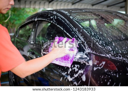 Closeup photo of man hand washing car with purple microfiber glove. Car wash with soap. Selective focus. Copy space.