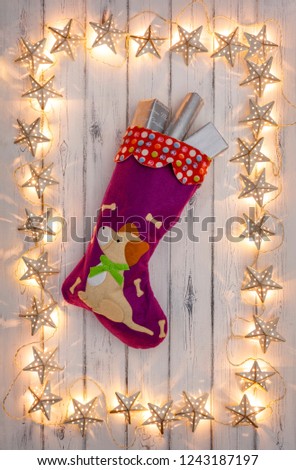 A border of golden star christmas lights, with a puppies christmas stocking and presents hanging in the middle, on a destressed woodern background
