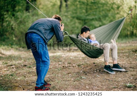 Photo shoot of dad and daughter outdoors on clear warm day. young photographer takes on camera of father and baby swinging in hammock