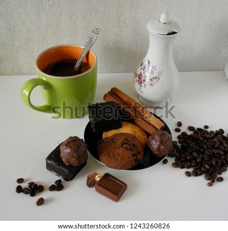 Cup and pot of coffee and coffee beans, cookies with cinnamon, chocolate candy, isolated on white.