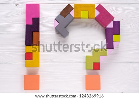 Exclamation point and a question mark from colorful wooden blocks on white wooden background.