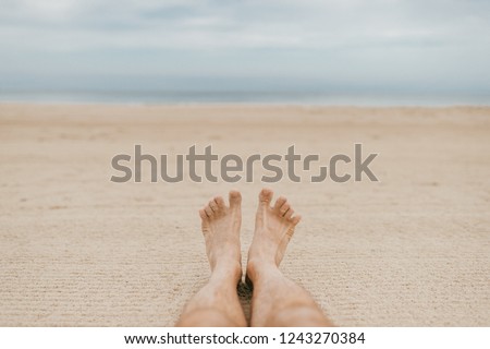 Men's feet on sandy beach. Rest on white sand on sea coast. Two legs of an adult male lying on loose sand by ocean