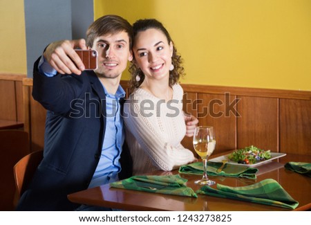 Positive young couple is photographed on a smartphone in a restaurant