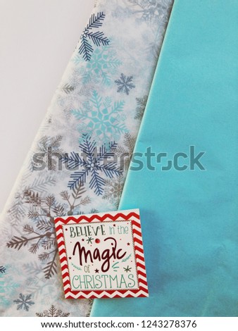 Christmas themed tissue wrapping paper and a gift card, with copy space. Believe in the Magic of Christmas.