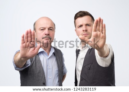 Two mature men giving showing stop hands gesture isolated on gray background. Need to make a stop at work.