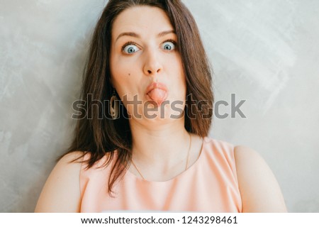 bright close up portrait pictures of teenage girl sticking out her tongue. funny young girl fooling around with tongue sticking out isolated on grey background