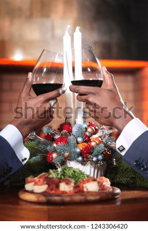 Two African American hands with glasses of red wine in focus. Hands raised on the background of the Christmas composition with candles. The concept of business meetings. New year.