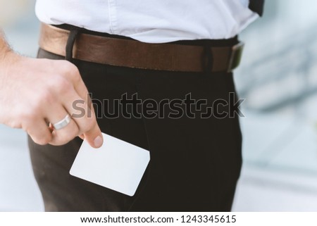 Male hand with white empty business card near pocket, close-up photo with selective focus. Horizontal placement