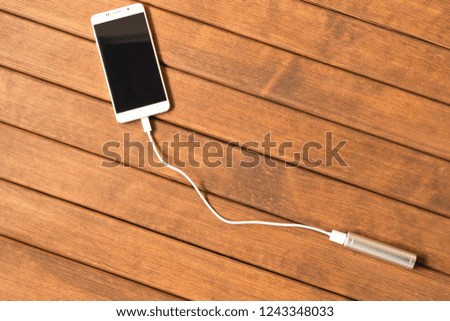 Silver power bank charging smartphone on wooden table.