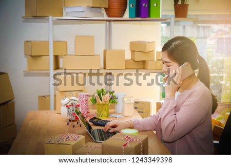 Concept Order Online : Business woman SME is in the midst of a telephone conversation with the customer and looking at a notebook computer to explain something, in the office home.
