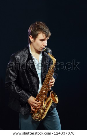 Studio portrait of happy young man with saxophone on dark background.