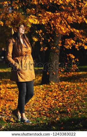 Outdoors lifestyle close up portrait of charming young woman wearing a wreath of autumn leaves. walking on the autumn park. Wreath of maple leaves
