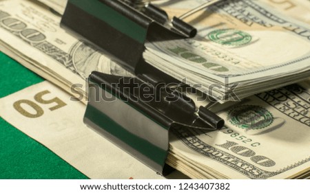 Stack of money with binder clips on green table, closeup.