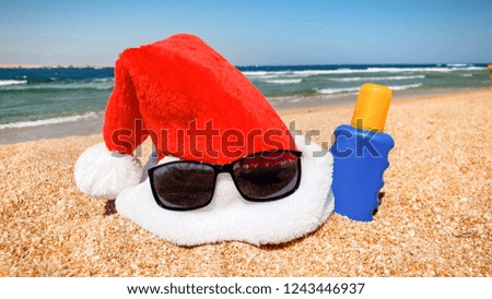 Closeup image of Santa's hat and sunglasses on the sea beach. Concept of travel and tourism on Christmas, New Year and winter holidays.