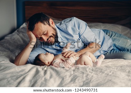 Portrait of middle age Caucasian father talking to newborn baby son daughter. Male man parent smiling to child on bed in bedroom at home. Authentic lifestyle real candid moment.  Royalty-Free Stock Photo #1243490731