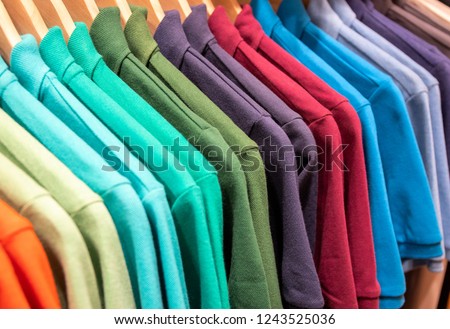 Vibrant shirts on hangs for sale in shop. Multicolored polo on wooden hanger. Summer fashion in department store. Unisex apparel for warm weather. Sale in shopping mall. Color gradient t-shirts Royalty-Free Stock Photo #1243525036