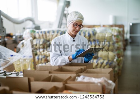 Female worker using tablet for checking boxes while standing in food factory.