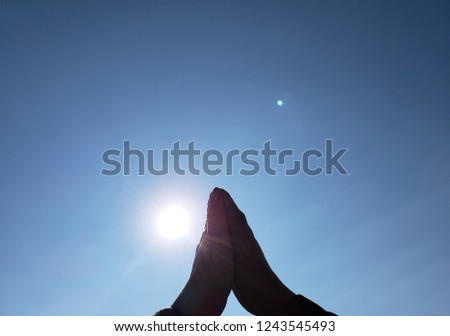 hands of a person in prayer position with the sun and the blue sky in the background